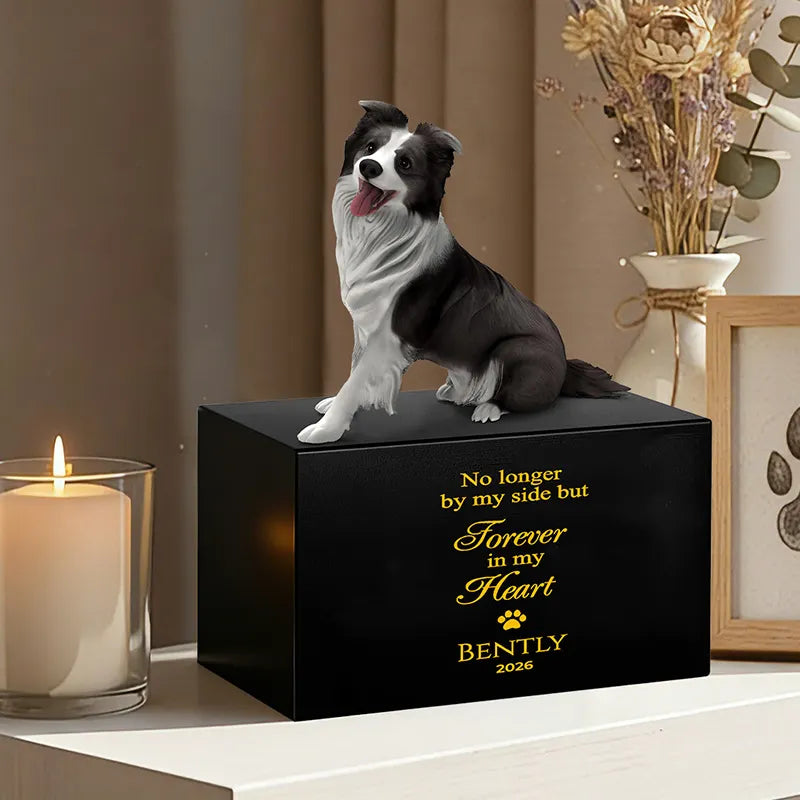 The PawPrint Dog Urn, a black custom pet urn with a 3D Border Collie figurine and gold text "No longer by my side but forever in my heart Bently 2026," sits beside a lit candle and framed art—a tasteful wooden memorial.