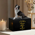 The PawPrint Dog Urn, a black custom pet urn with a 3D Border Collie figurine and gold text "No longer by my side but forever in my heart Bently 2026," sits beside a lit candle and framed art—a tasteful wooden memorial.