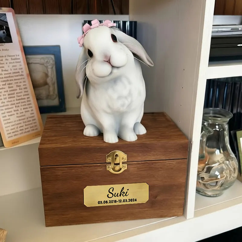 The Bunny Sweet Memories features a 3D printed rabbit statue with a pink bow on a wooden box engraved "Suki 03.08.2016–12.03.2024," displayed on a bookshelf with books and a glass jar.